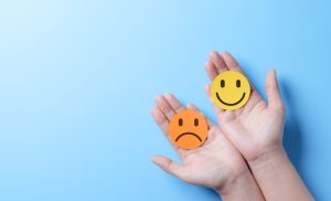 a pair of hands holding a sad face emoji and a happy face emoji