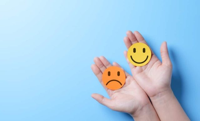 a pair of hands holding a sad face emoji and a happy face emoji