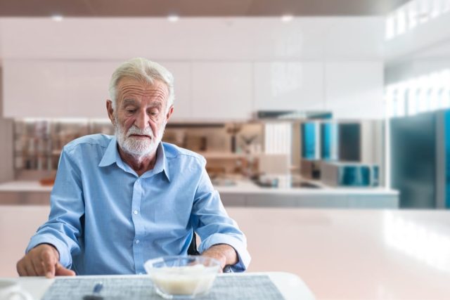 Senior man sitting quietly at a kitchen table looking uninterested in his meal